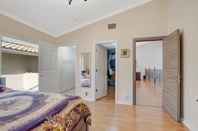 bedroom featuring visible vents, lofted ceiling, a walk in closet, crown molding, and light wood-type flooring