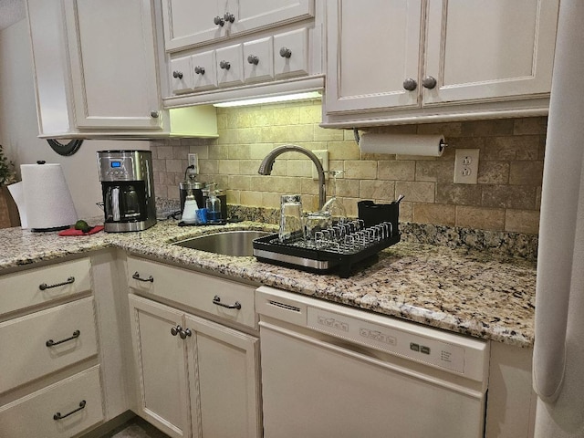 kitchen featuring backsplash, light stone countertops, dishwashing machine, white cabinets, and a sink