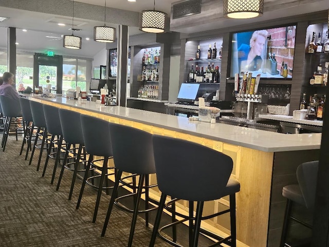 bar featuring decorative light fixtures, visible vents, carpet flooring, and a community bar