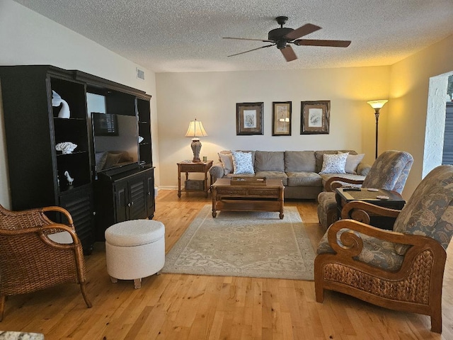 living room with light wood finished floors, visible vents, a textured ceiling, and ceiling fan