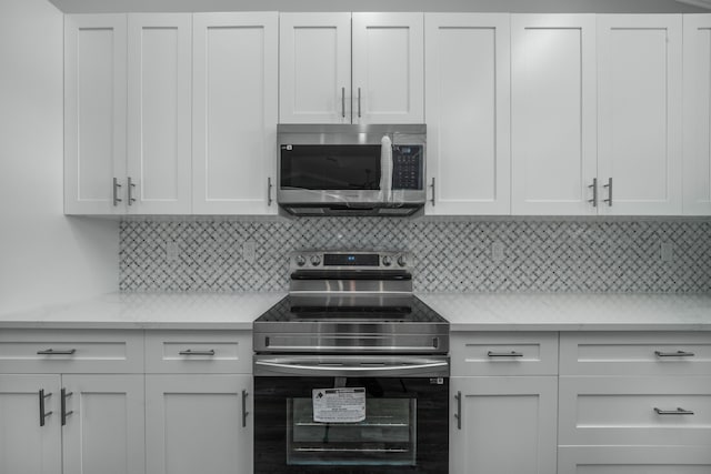 kitchen featuring tasteful backsplash, white cabinets, stainless steel appliances, and light countertops