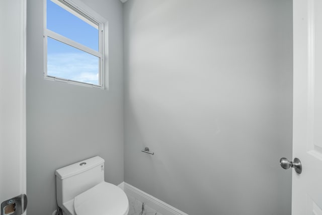 bathroom with baseboards, toilet, and marble finish floor