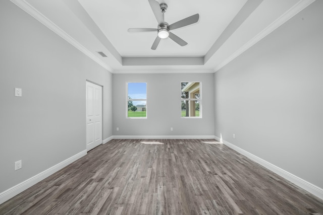 empty room with baseboards, a raised ceiling, visible vents, and wood finished floors