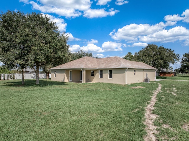 rear view of property featuring central air condition unit, a lawn, stucco siding, and fence