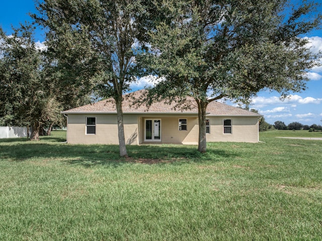 back of house with stucco siding, a yard, and fence