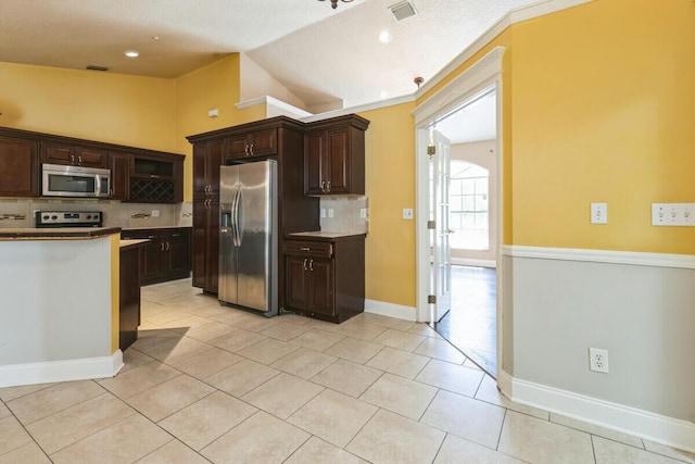 kitchen featuring tasteful backsplash, dark brown cabinetry, appliances with stainless steel finishes, light tile patterned floors, and lofted ceiling