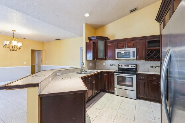 kitchen featuring light tile patterned floors, a peninsula, a sink, light countertops, and appliances with stainless steel finishes