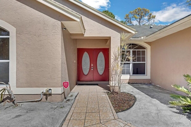 view of exterior entry with a shingled roof and stucco siding