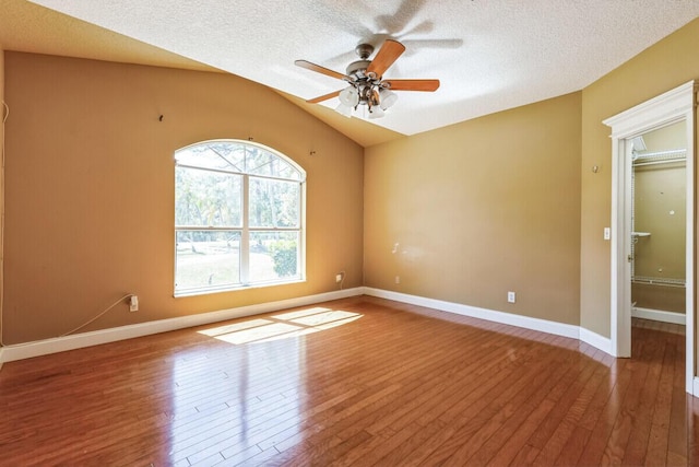 empty room featuring vaulted ceiling, hardwood / wood-style flooring, a ceiling fan, and a textured ceiling