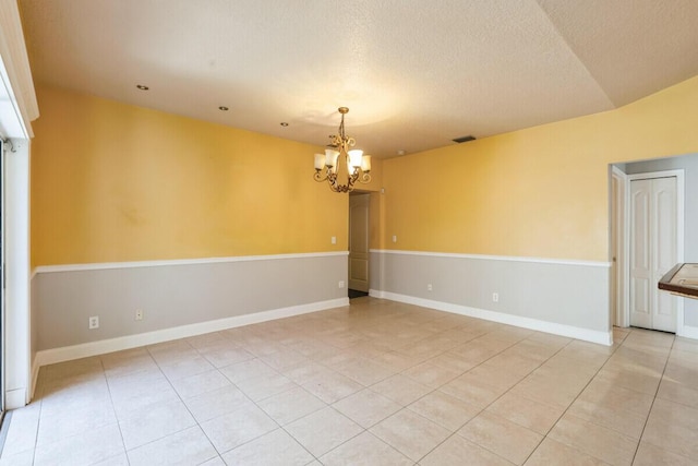 spare room featuring visible vents, a textured ceiling, light tile patterned floors, baseboards, and a chandelier