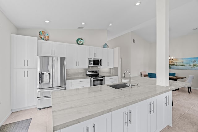 kitchen with lofted ceiling, appliances with stainless steel finishes, light tile patterned flooring, white cabinets, and a sink