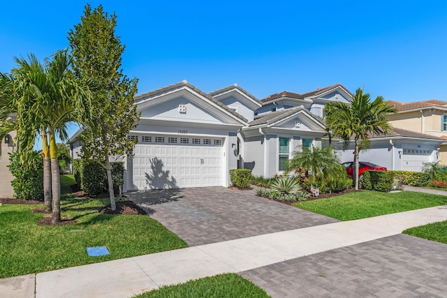 view of front of home with stucco siding, a front lawn, decorative driveway, an attached garage, and a tiled roof