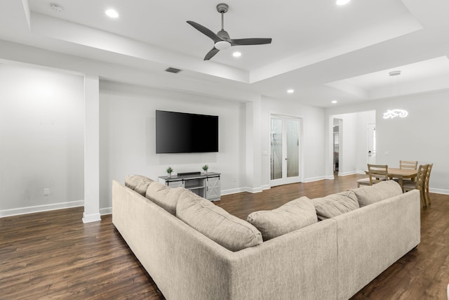 living room with a raised ceiling, baseboards, and dark wood-type flooring