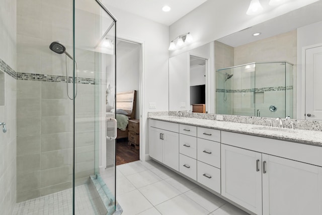 ensuite bathroom with connected bathroom, double vanity, a stall shower, tile patterned floors, and a sink