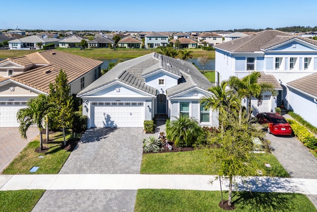 view of front of property featuring a front lawn, decorative driveway, a residential view, a garage, and a tiled roof