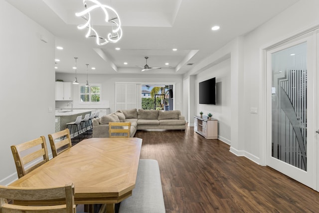 dining room with a raised ceiling, dark wood-type flooring, ceiling fan with notable chandelier, recessed lighting, and baseboards