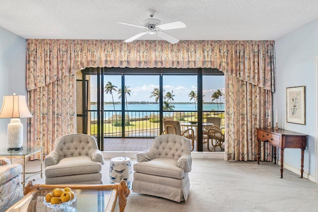 sitting room featuring a ceiling fan, baseboards, carpet floors, a water view, and a textured ceiling