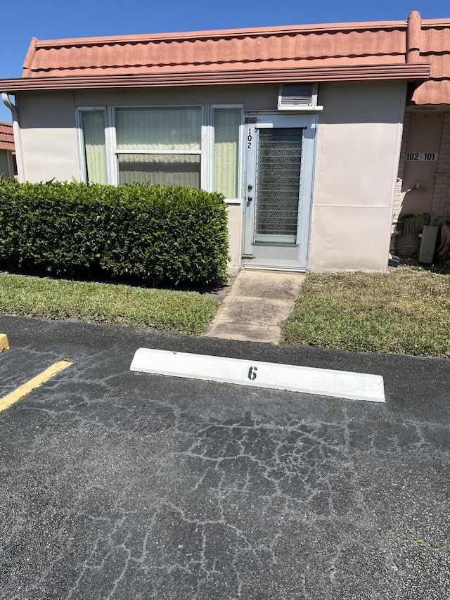 property entrance with stucco siding, a tile roof, and uncovered parking