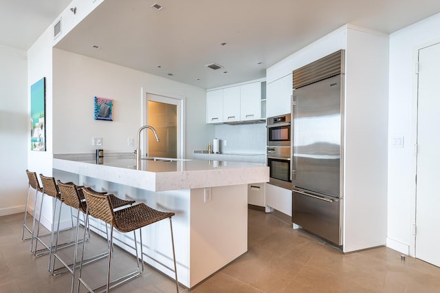 kitchen featuring visible vents, a kitchen bar, white cabinets, stainless steel appliances, and a sink