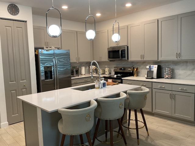 kitchen with backsplash, gray cabinets, appliances with stainless steel finishes, and light wood-type flooring