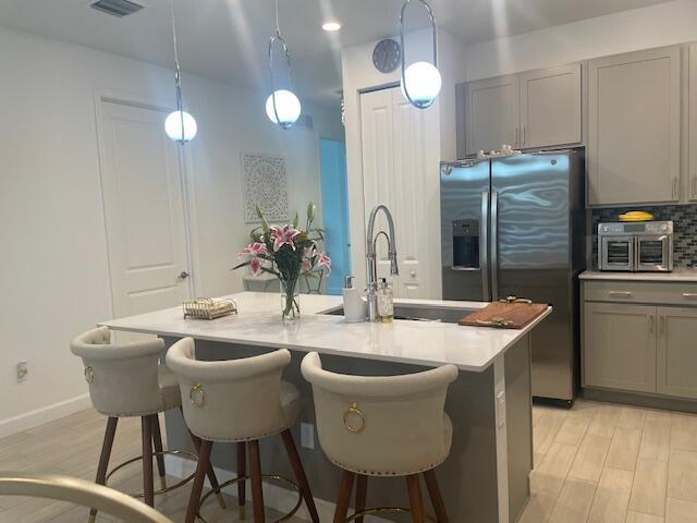 kitchen featuring tasteful backsplash, a breakfast bar, light countertops, gray cabinets, and stainless steel refrigerator with ice dispenser