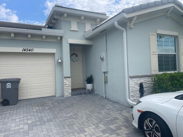 view of side of home featuring stucco siding, stone siding, an attached garage, and decorative driveway