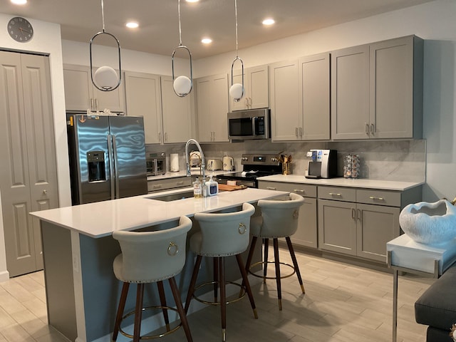 kitchen with light wood-style flooring, a sink, gray cabinetry, appliances with stainless steel finishes, and backsplash