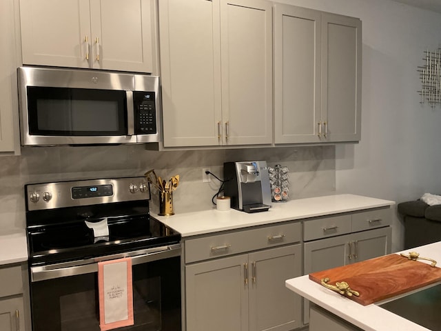 kitchen featuring stainless steel appliances, decorative backsplash, gray cabinets, and light countertops