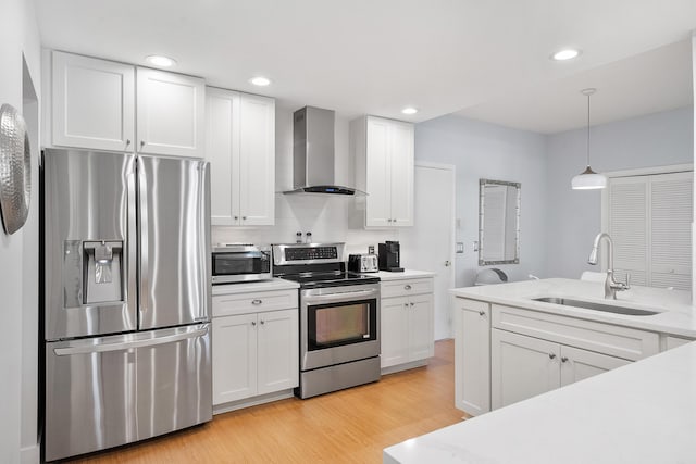 kitchen featuring light wood-type flooring, a sink, stainless steel appliances, wall chimney exhaust hood, and light countertops