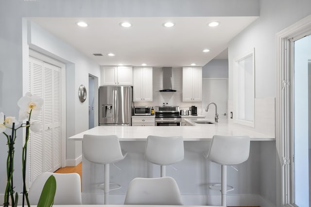 kitchen featuring a breakfast bar, wall chimney exhaust hood, appliances with stainless steel finishes, and a sink