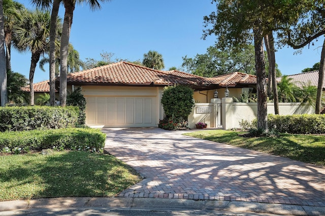 mediterranean / spanish home with a fenced front yard, a tile roof, stucco siding, a garage, and driveway