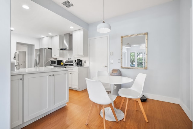 kitchen with light wood finished floors, visible vents, wall chimney range hood, appliances with stainless steel finishes, and white cabinets