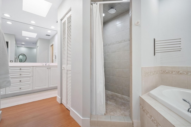 bathroom featuring vanity, a skylight, a bath, and tiled shower