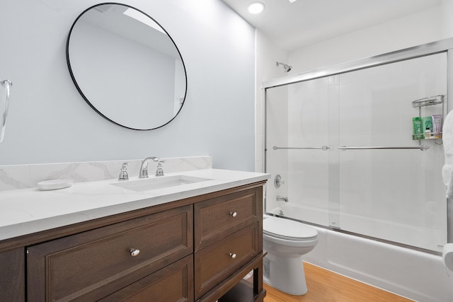 full bathroom featuring wood finished floors, toilet, vanity, and bath / shower combo with glass door