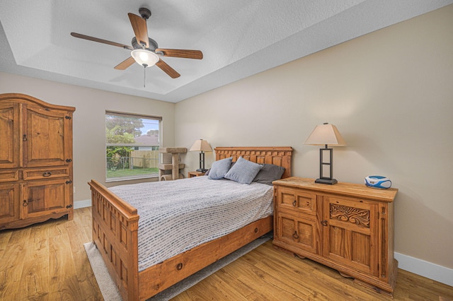 bedroom with light wood-type flooring, a raised ceiling, and baseboards