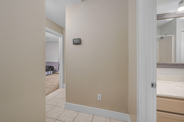 corridor featuring light tile patterned floors, a textured ceiling, and baseboards