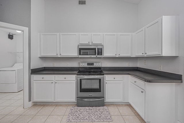 kitchen featuring dark countertops, appliances with stainless steel finishes, light tile patterned flooring, and white cabinets