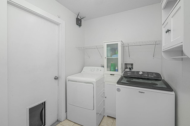 laundry room featuring a textured ceiling, light tile patterned floors, cabinet space, and washer and clothes dryer