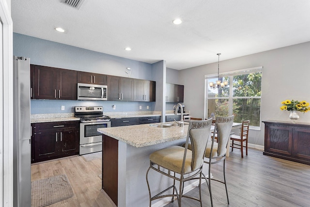 kitchen featuring dark brown cabinets, light wood-style flooring, a kitchen breakfast bar, stainless steel appliances, and a sink