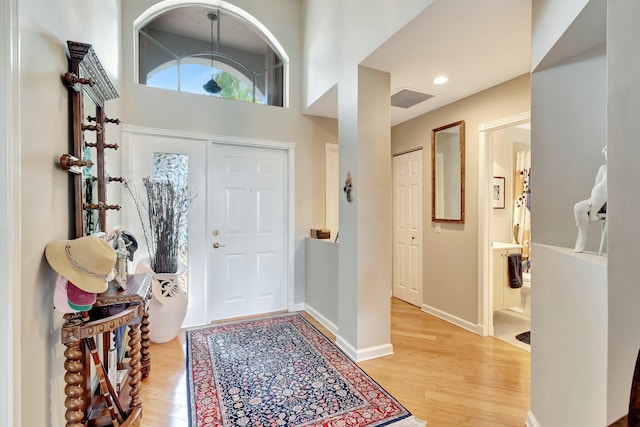 foyer entrance featuring visible vents, baseboards, light wood-style floors, and a towering ceiling