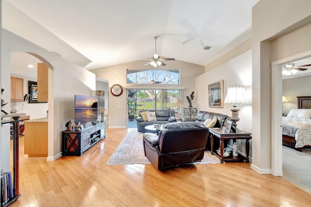 living area with light wood-type flooring, visible vents, arched walkways, lofted ceiling, and ceiling fan