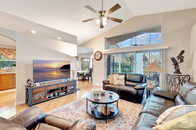 living area featuring a ceiling fan, baseboards, light wood finished floors, high vaulted ceiling, and arched walkways