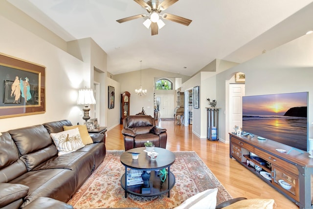 living room featuring ceiling fan with notable chandelier, light wood-style flooring, baseboards, and vaulted ceiling