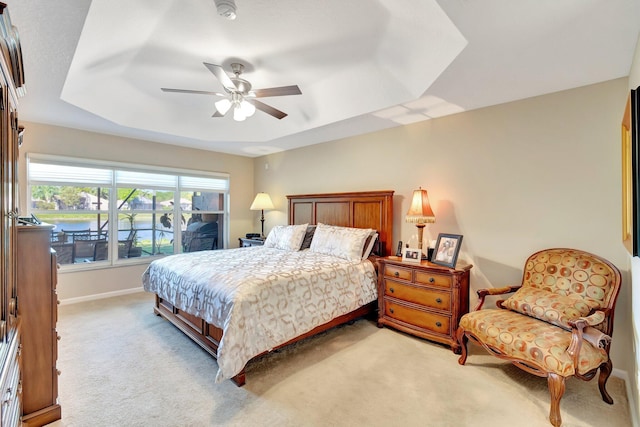 bedroom featuring ceiling fan, a raised ceiling, baseboards, and light carpet