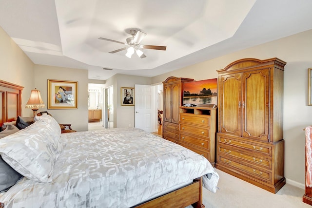 carpeted bedroom featuring visible vents, ensuite bathroom, a tray ceiling, baseboards, and ceiling fan