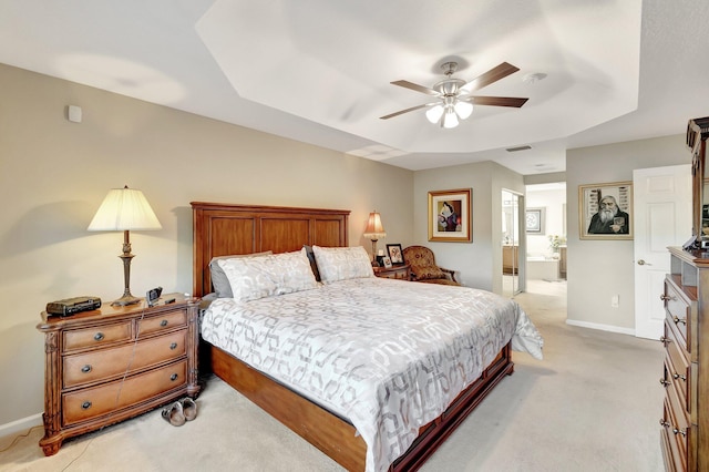 bedroom with ensuite bath, a raised ceiling, baseboards, and light carpet