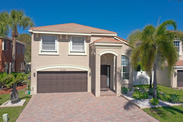 mediterranean / spanish house with fence, a tiled roof, stucco siding, decorative driveway, and a garage