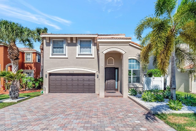 mediterranean / spanish-style home featuring stucco siding, decorative driveway, fence, a garage, and a tiled roof