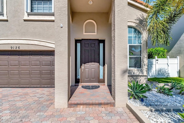 entrance to property featuring fence, a garage, and stucco siding