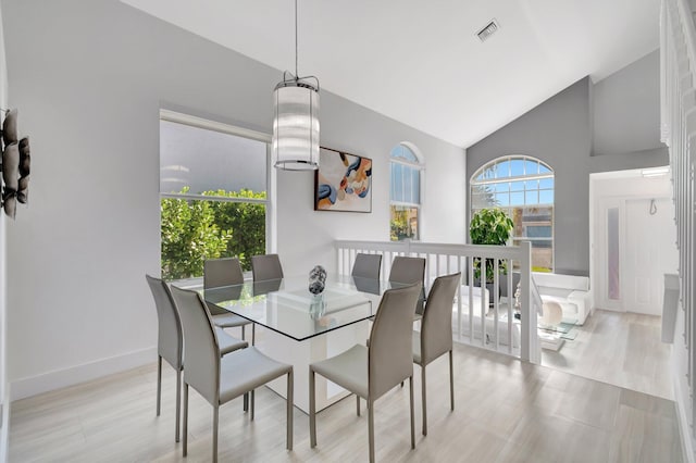 dining space with visible vents, light wood-type flooring, baseboards, and vaulted ceiling